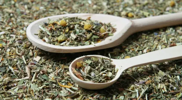 Zwei Holzlöffel gefüllt mit Kräutern für Tee selber machen Rezepte. Die Mischung duftet nach Kamille und anderen Heilkräutern.