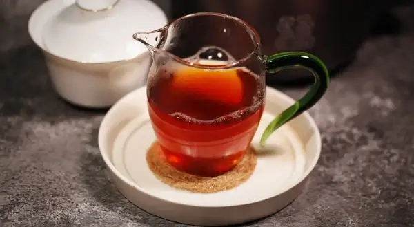 Ein Glas mit Oolong Tee, dessen Farbe an einen Krebs erinnert, steht auf einem Untersetzer. Daneben eine weiße Teedose.
