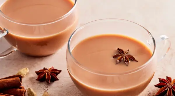 Zwei Tassen cremiger Chai Latte, garniert mit Sternanis. Zimtstangen und Kardamomkapseln deuten auf ein authentisches indischer chai rezept hin.