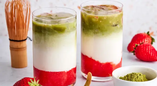 Zwei Schichten-Getränke mit Erdbeerpüree, Milch und Matcha. Ein Chasen und frische Erdbeeren deuten an, was ist eigentlich in rotem Matcha drin.