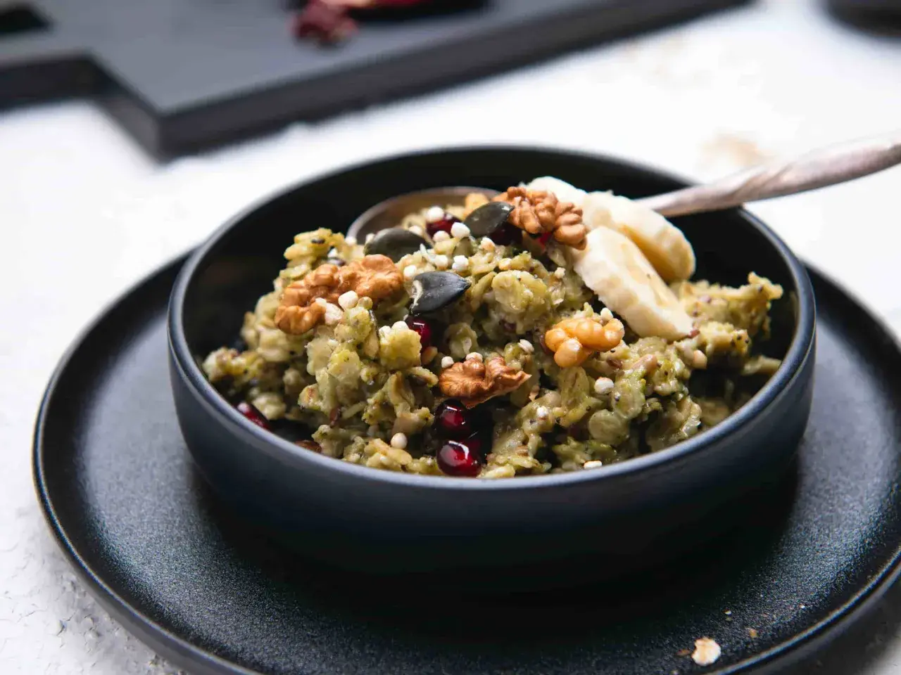 Grüner, cremiger matcha porridge mit Nüssen, Kernen, Granatapfel und Bananenscheiben. Ein gesundes Frühstück.