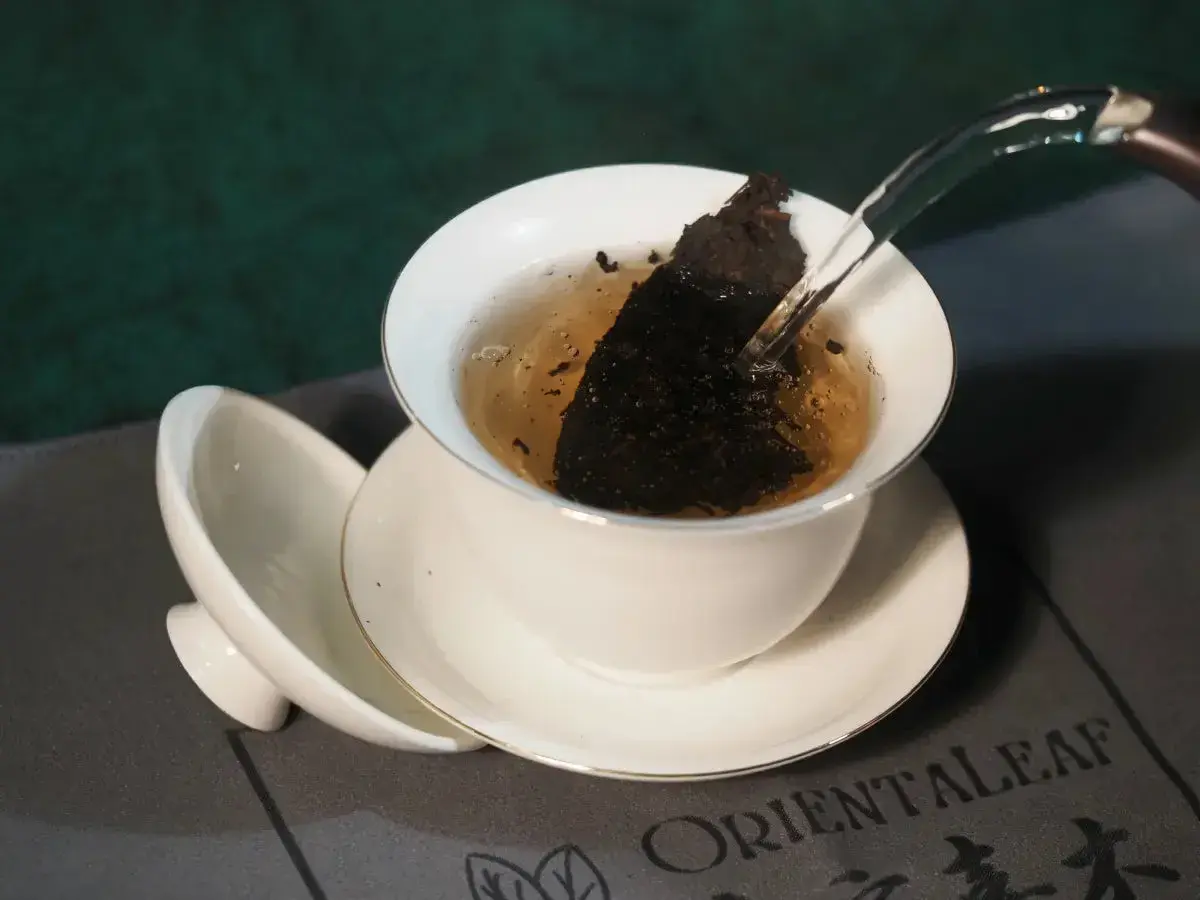 Heißes Wasser fließt in eine Teetasse mit Pu-erh Tee. Mögliche Pu-erh Tee Nebenwirkungen sind selten, aber bei übermäßigem Genuss zu beachten.