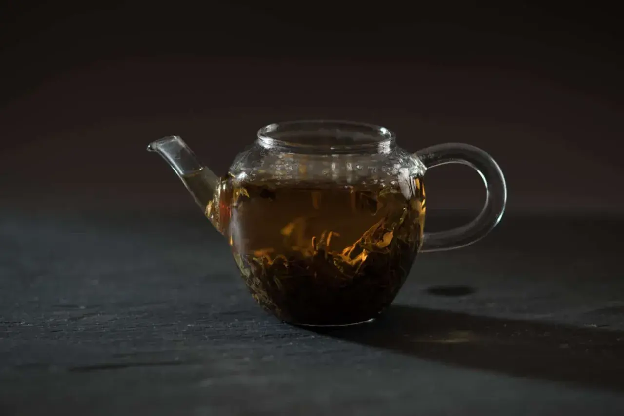 Glas-Teekanne mit braunem Tee und sichtbaren Tee-Inhaltsstoffen.