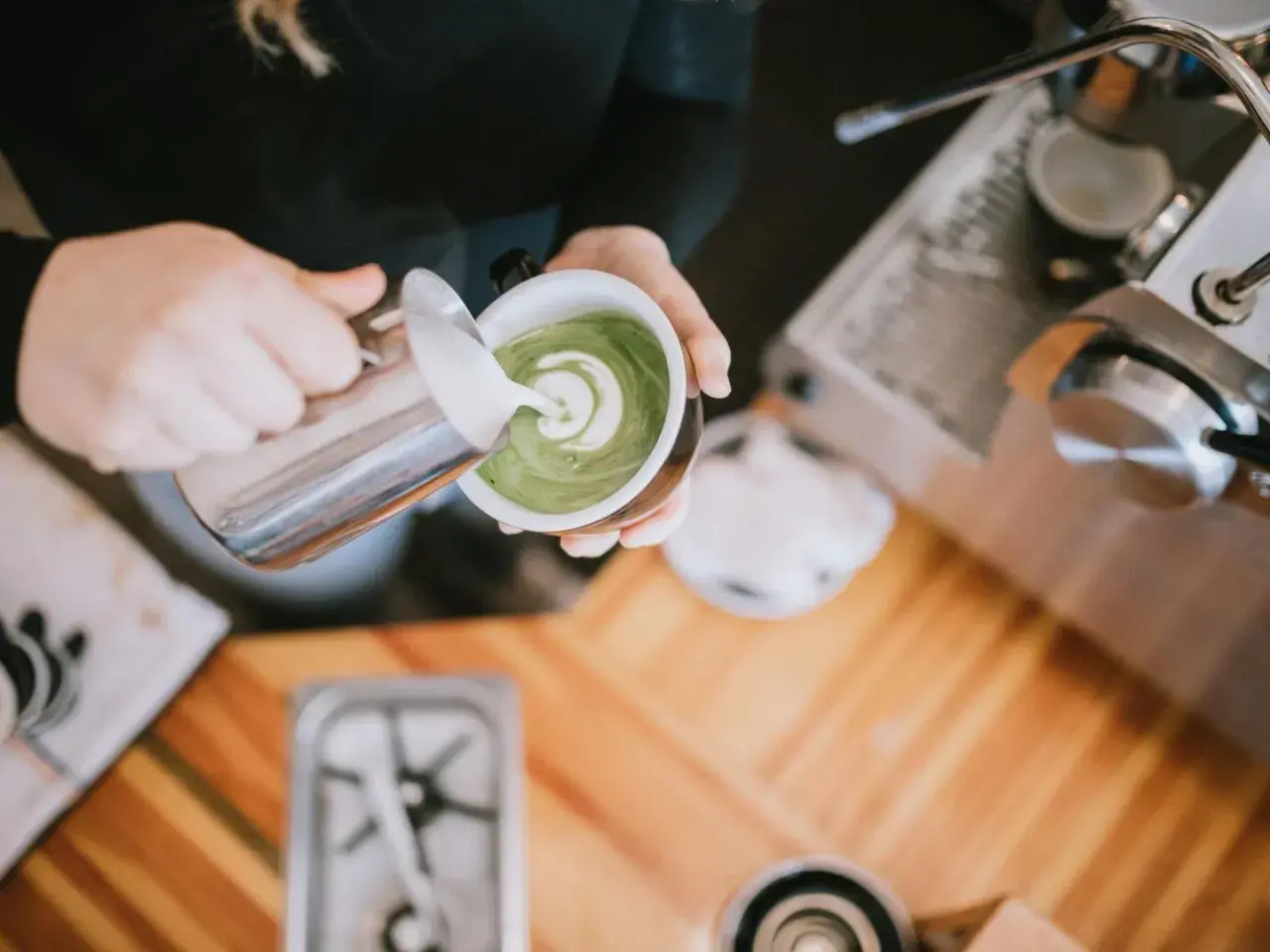 Barista verziert grünen Matcha-Tee mit Milchschaum. Perfekt für den Start in den Tag, auch auf leeren Magen.