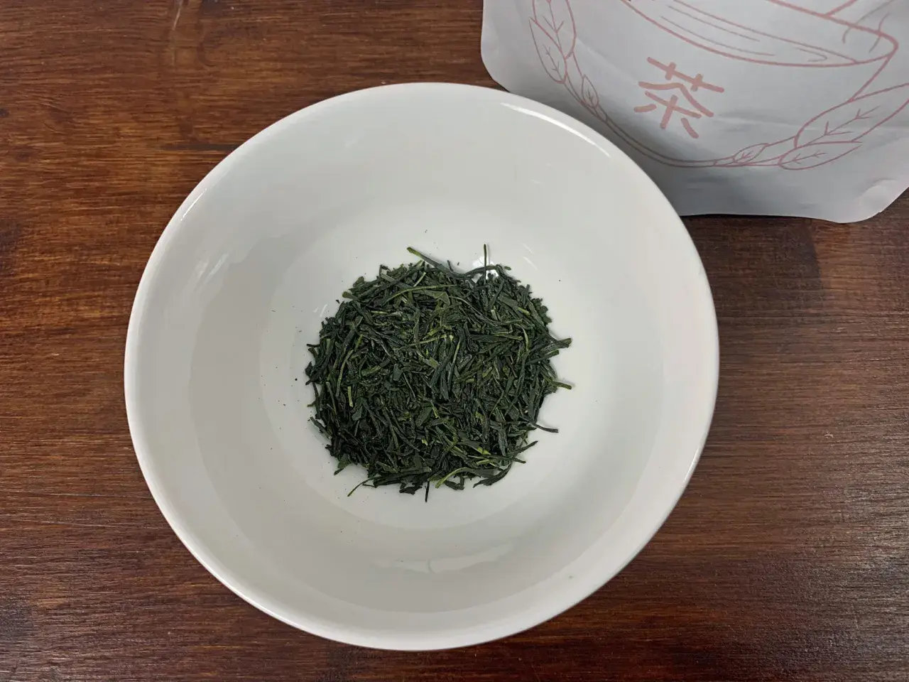 Trockene, dunkelgrüne Sencha-Teeblätter liegen in einer weißen Schale, bereit für die Zubereitung.