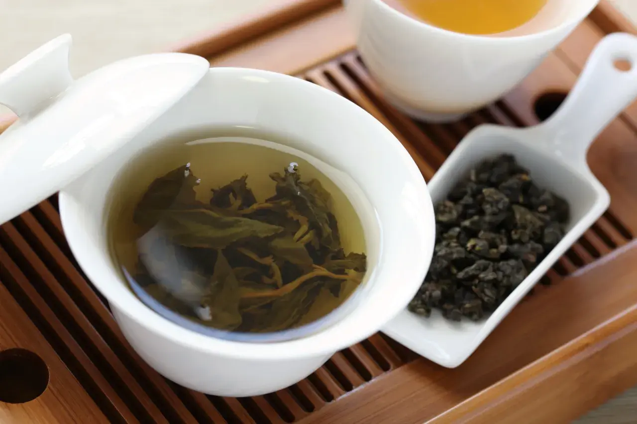 Eine Tasse Oolong Tee, daneben trockene Blätter. Wie viel Oolong Tee am Tag ist gesund?
