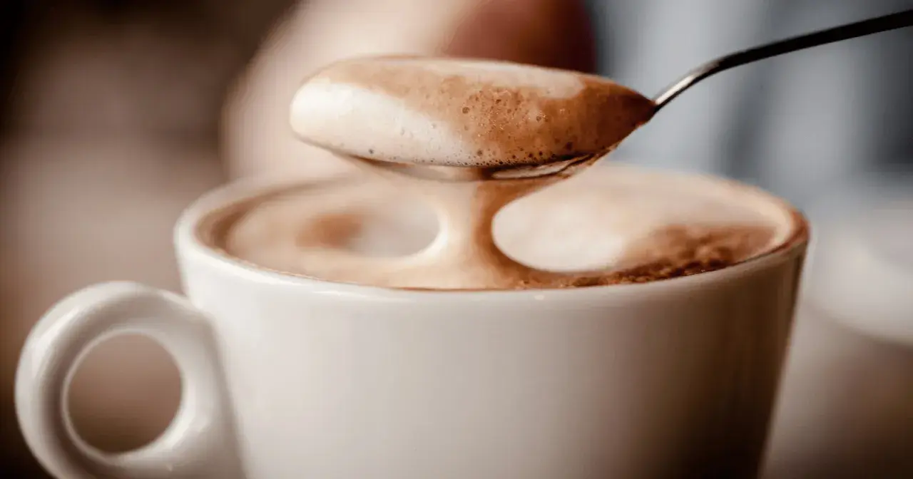 Ein Löffel voller Milchschaum über einer Tasse Kaffee. Der Koffein-Kick für den Magen.