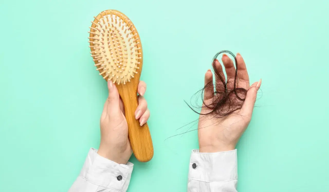 Hände halten Haarbürste und Haarbüschel. Ein Zeichen für Haarausfall, vielleicht nach dem Genuss von schwarzem Tee?
