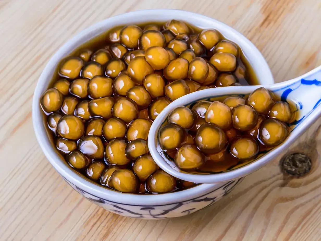 Ein Schälchen mit braunen Tapiokaperlen, perfekt für ein leckeres Boba-Rezept. Eine Löffel voller Perlen zeigt die köstliche Textur.