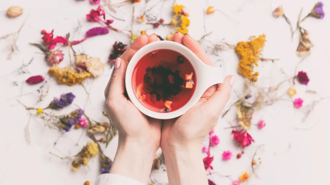 Hände halten eine Tasse mit rotem Tee, umgeben von getrockneten Blumen. Ein perfekter Tee am Morgen für einen frischen Start.