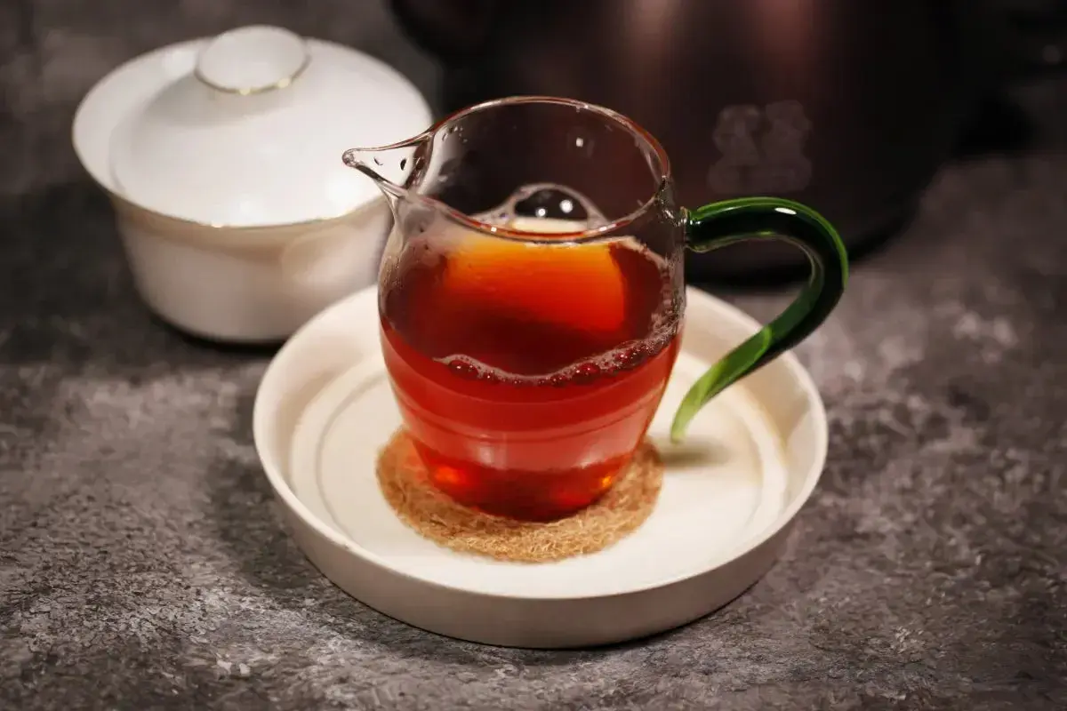 Ein Glas mit Oolong Tee, dessen Farbe an einen Krebs erinnert, steht auf einem Untersetzer. Daneben eine weiße Teedose.