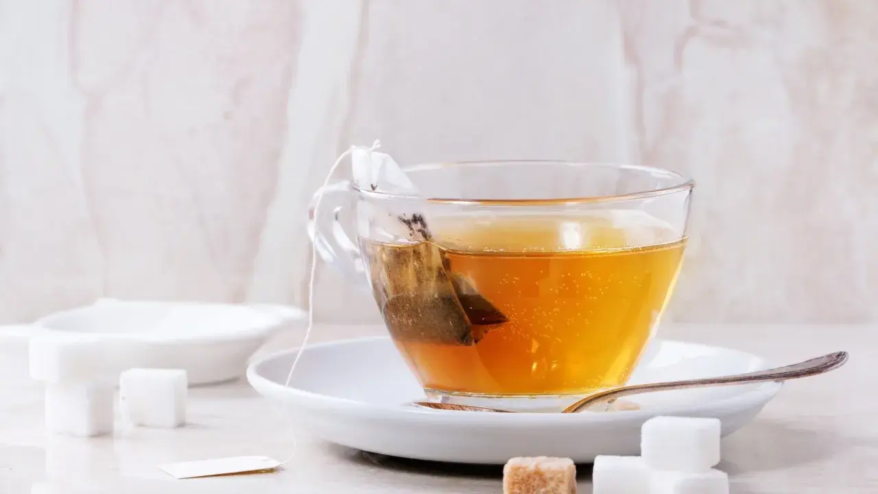 Eine Tasse Tee mit einem Teebeutel, der aussieht, als wäre der abgelaufene Tee schon lange im Wasser. Zuckerwürfel liegen daneben.