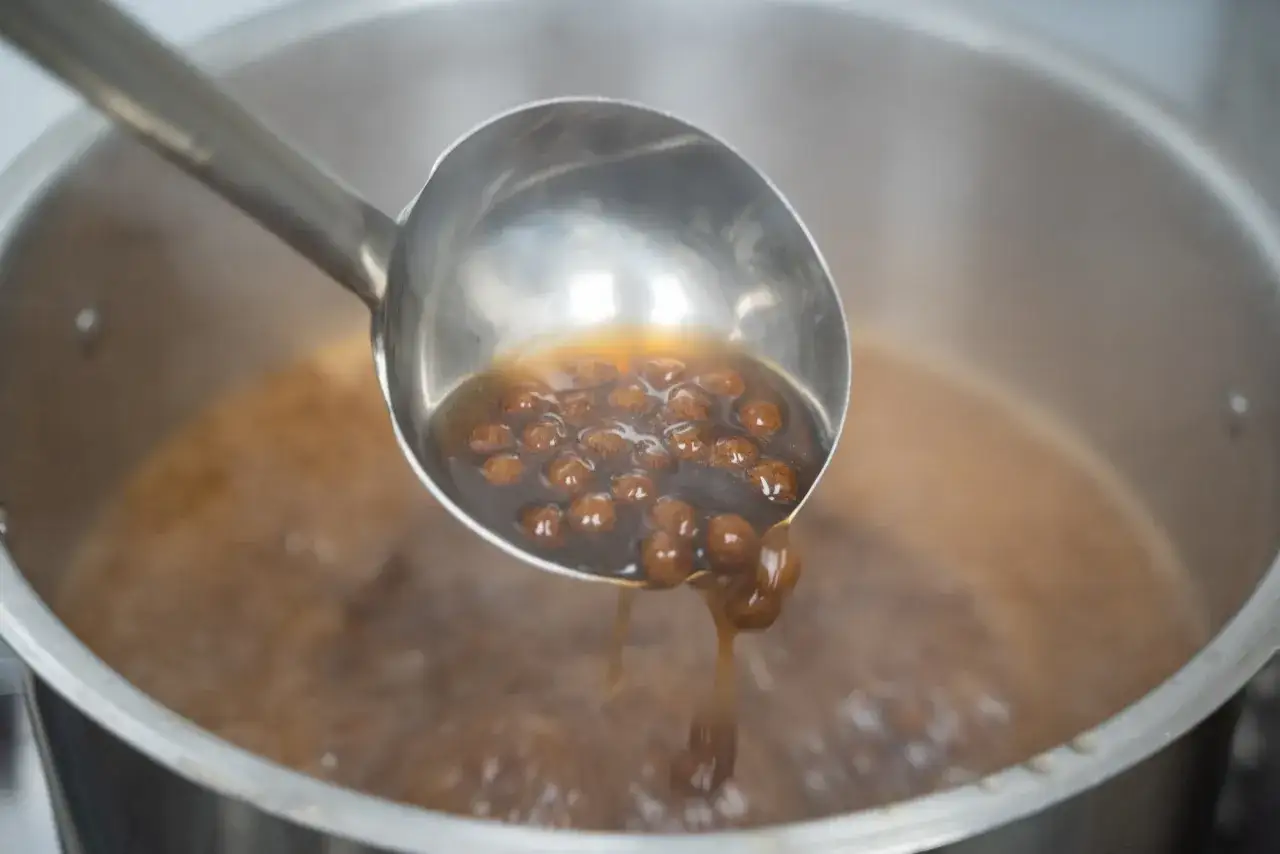 Boba-Perlen werden mit einer Sch&ouml;pfkelle aus einem Topf mit kochender Fl&uuml;ssigkeit entnommen. Ein Schritt im perfekten boba rezept.