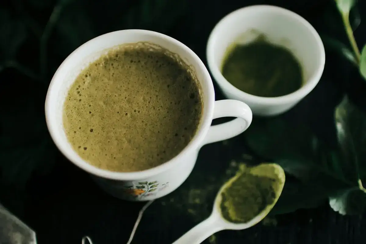 Eine Tasse cremiger Matcha, bereit f&uuml;r den Start in den Tag auf leeren Magen. Daneben eine kleine Schale mit Matcha-Pulver und ein L&ouml;ffel voller gr&uuml;ner Energie.