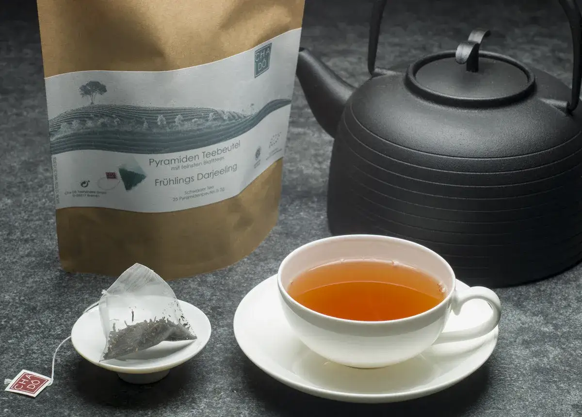 Eine Tasse Darjeeling Tee, die erste Ernte (first flush bedeutung) des Jahres, duftet neben einer Teekanne und einem Beutel.
