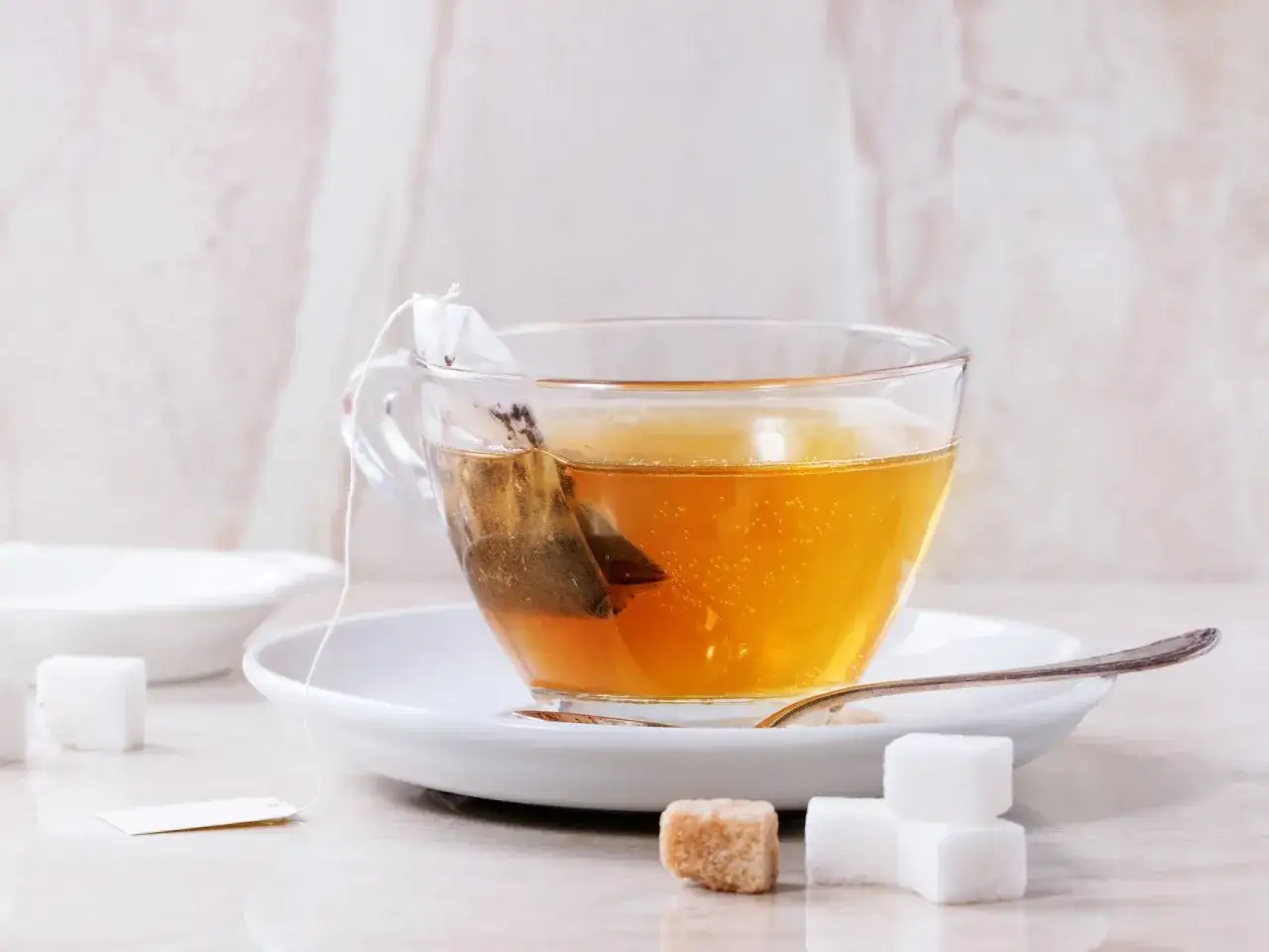 Eine Tasse Tee mit einem Teebeutel, daneben Zuckerw&uuml;rfel. Der Tee sieht aus, als w&auml;re er abgelaufener Tee, der nicht mehr frisch ist.