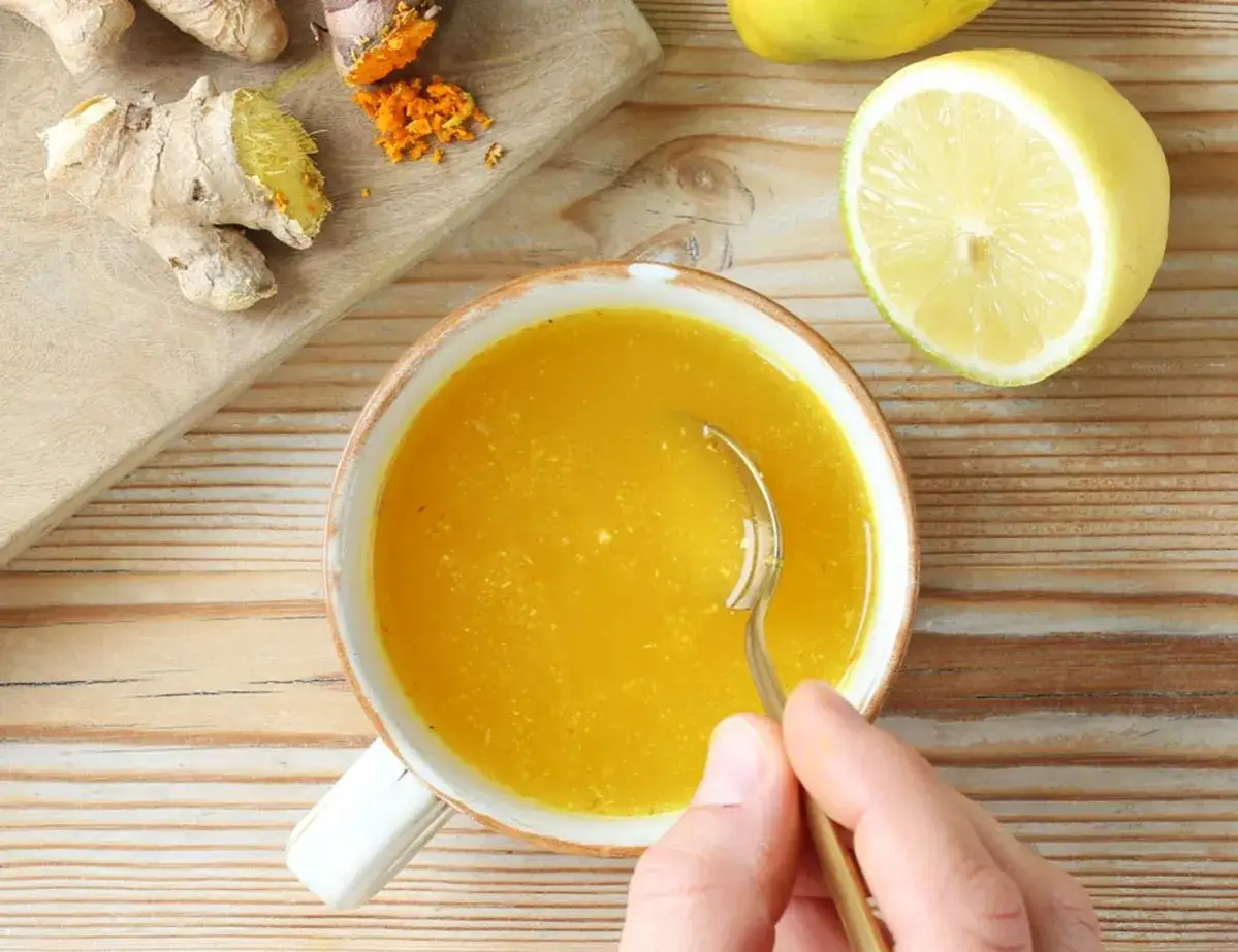 Gesunde Getränke mit Kurkuma und Ingwer: Eine Tasse goldener Trank, daneben frische Zitronen und Wurzeln. Perfekt für Rezepte mit Kurkuma und Ingwer.