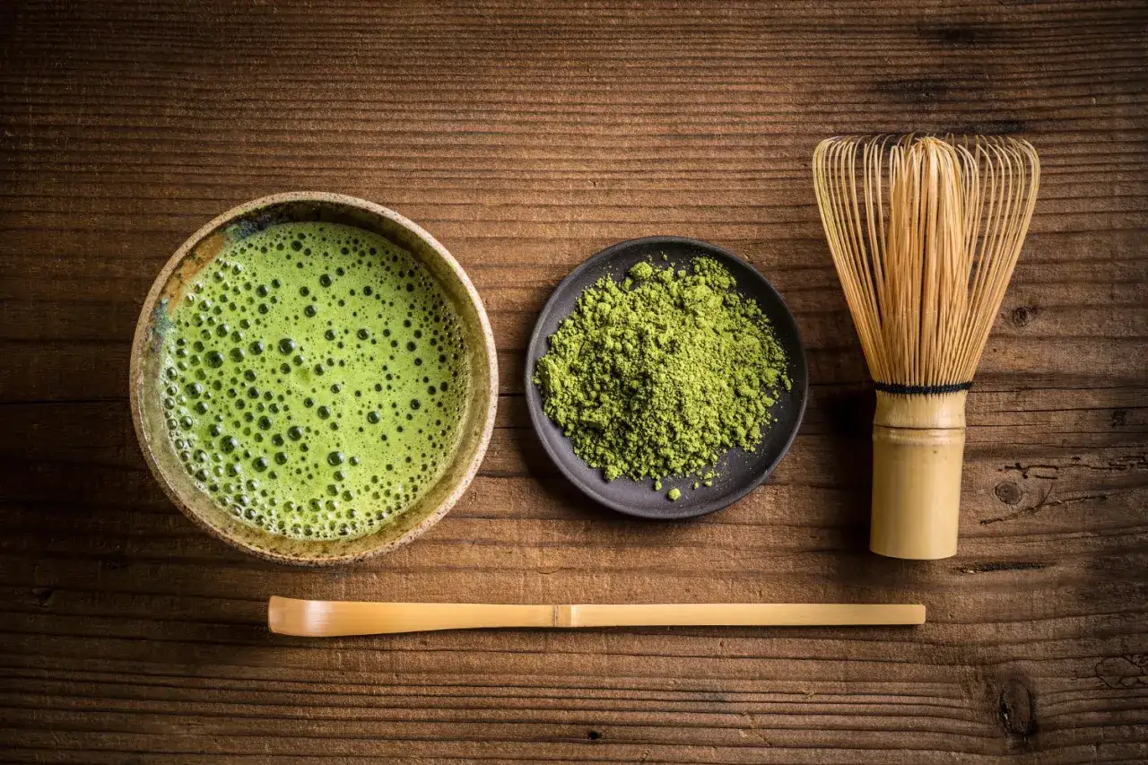 Matcha-Zubereitung: Eine Schale mit schaumigem Matcha, daneben Pulver und ein Chasen. Die ideale matcha temperatur ist entscheidend f&uuml;r den Geschmack.