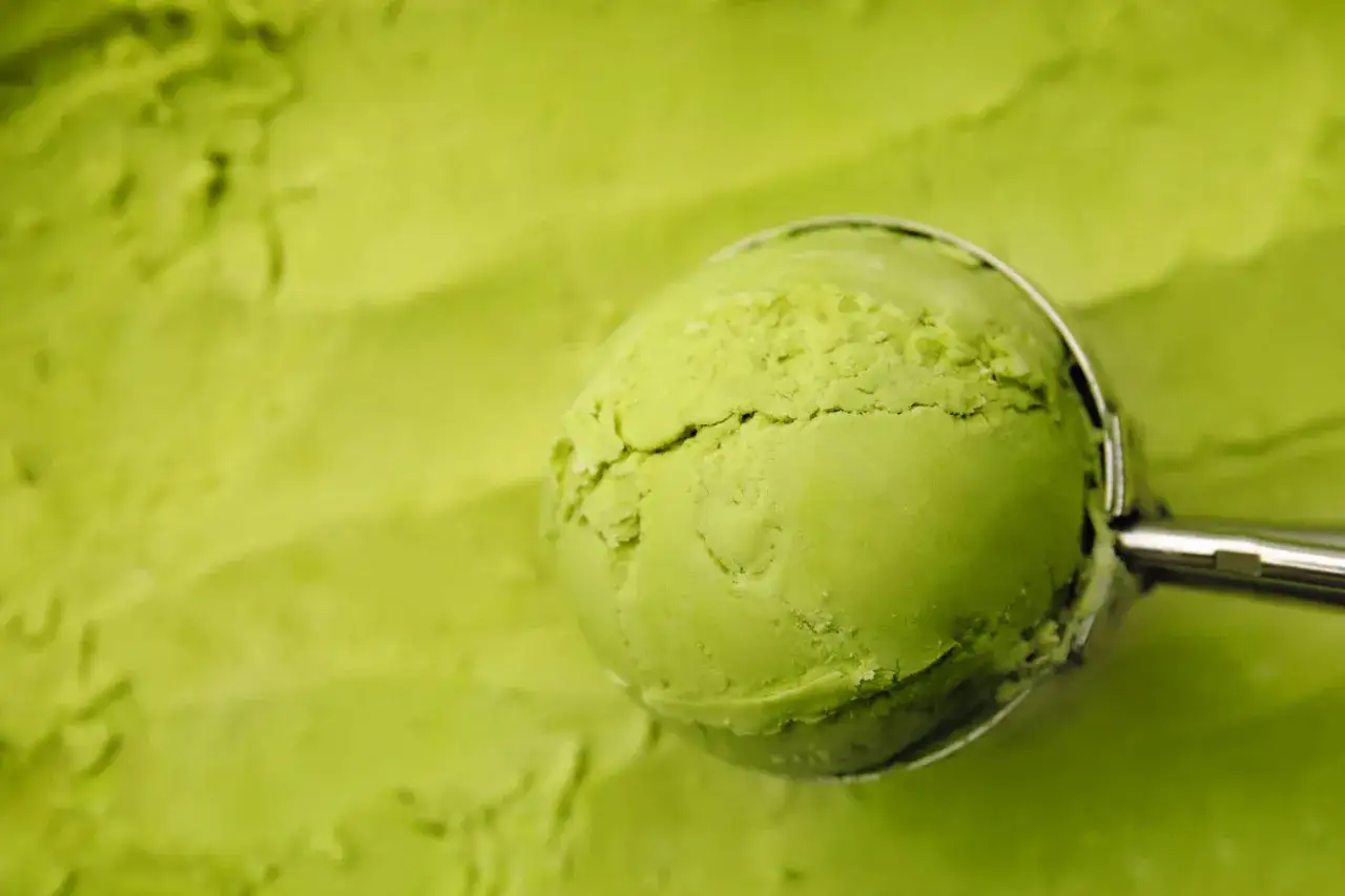 Ein L&ouml;ffel hebt eine Kugel cremiges, leuchtend gr&uuml;nes Matcha-Eis aus einer Sch&uuml;ssel.