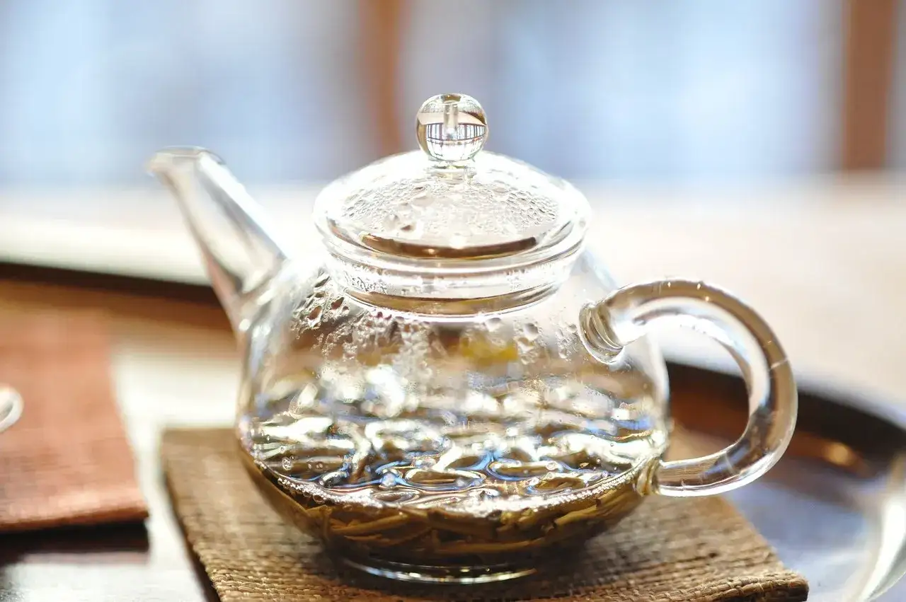 Glas-Teekanne mit Jasmintee-Bl&auml;ttern, bereit f&uuml;r die Zubereitung. Dampf steigt auf, ein Zeichen f&uuml;r die bevorstehende aromatische Tasse.