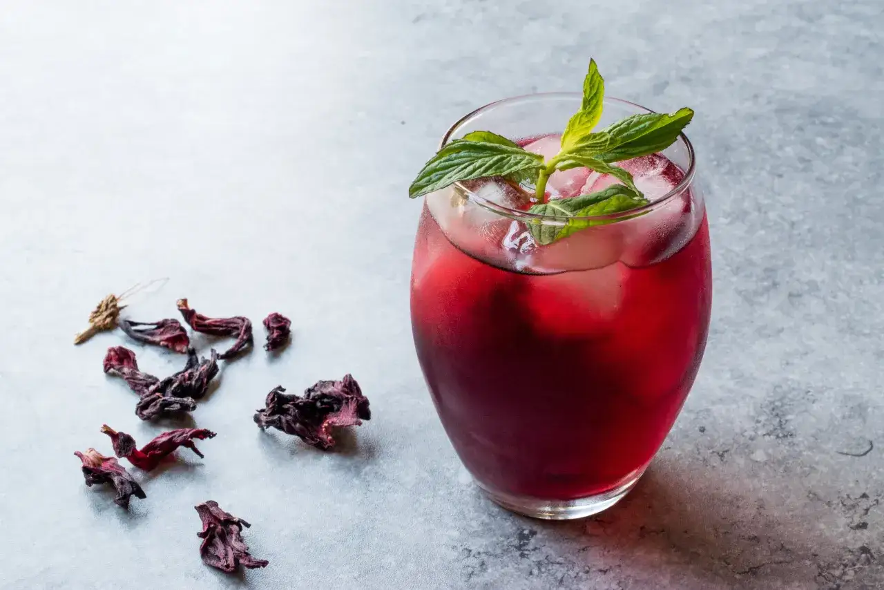 Erfrischendes Hibiskusgetränk mit Minze und Eis. Trockene Hibiskusblüten daneben deuten auf leckere Hibiskus Rezepte hin.