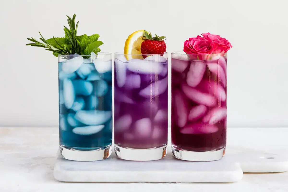 Drei bunte Eistees, blau, lila und pink, mit Eisw&uuml;rfeln und Garnituren. Die Zubereitung von Anchan Tee ist einfach und erfrischend.