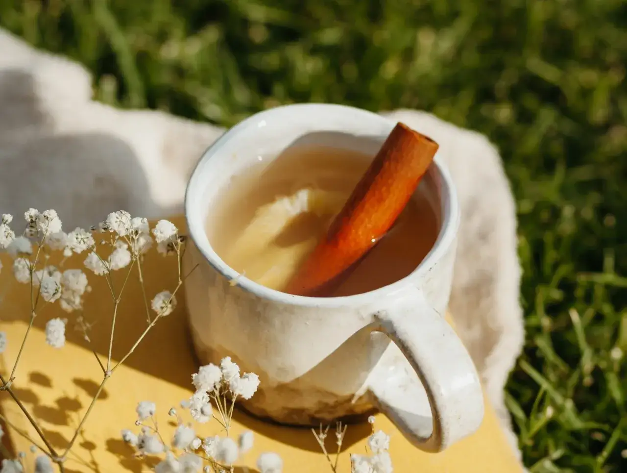 Eine Tasse mit warmem Getr&auml;nk und Zimtstange, daneben zarte wei&szlig;e Bl&uuml;ten. Perfekt, um zimt-tee selber machen mit pulver zu genie&szlig;en.