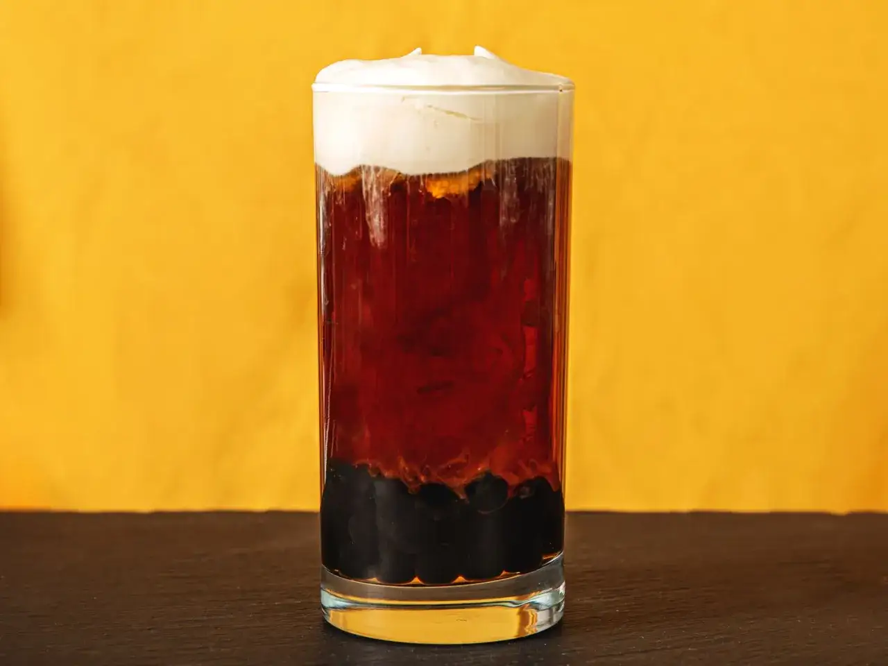 Ein Glas mit dunklem Tee, schwarzen Tapiokaperlen und einer cremigen K&auml;seschicht obendrauf. Ein erfrischender Cheese Tea.