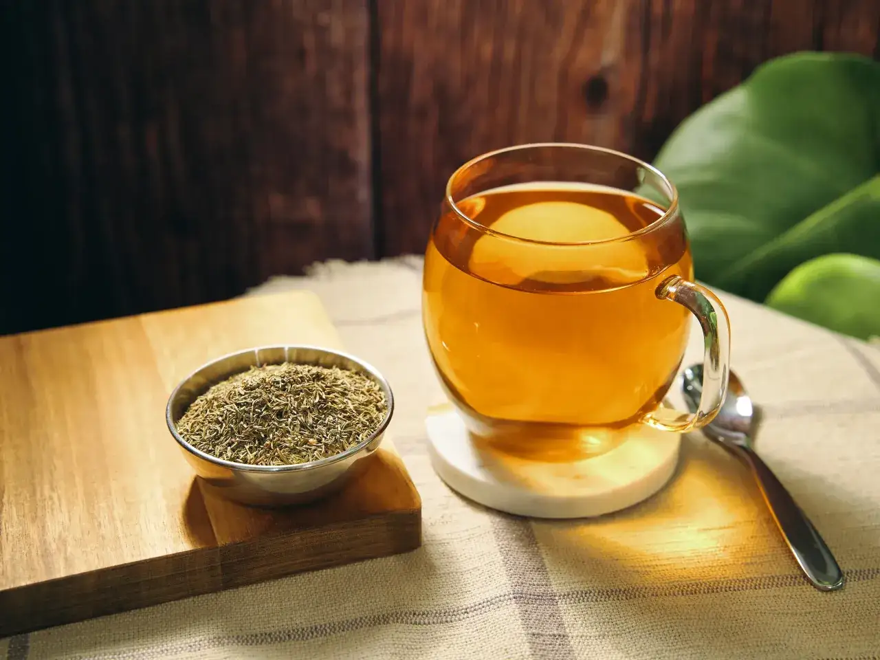 Ein Glas goldener Thymiantee steht neben einer Schale getrocknetem Thymian. Die Thymiantee Wirkung ist bekannt für ihre beruhigenden Eigenschaften.