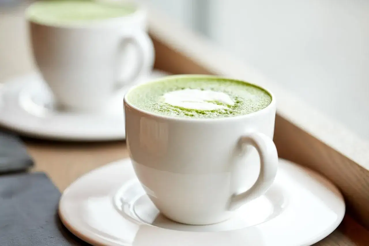 Zwei wei&szlig;e Tassen mit cremigem Matcha-Latte. Eine sanfte Wahl f&uuml;r die matcha schwangerschaft.