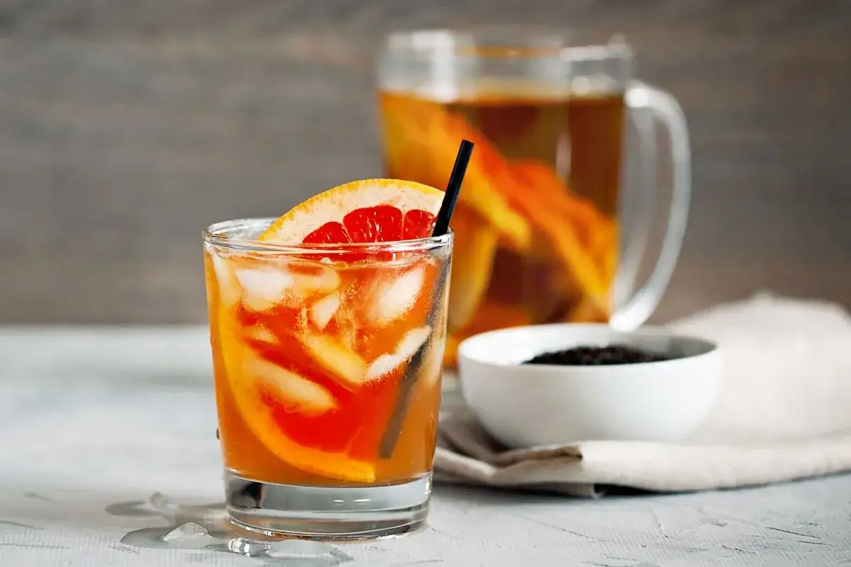 Erfrischender Gin mit Eistee, Eiswürfeln und Grapefruit-Scheiben. Im Hintergrund eine Karaffe mit dem Getränk.