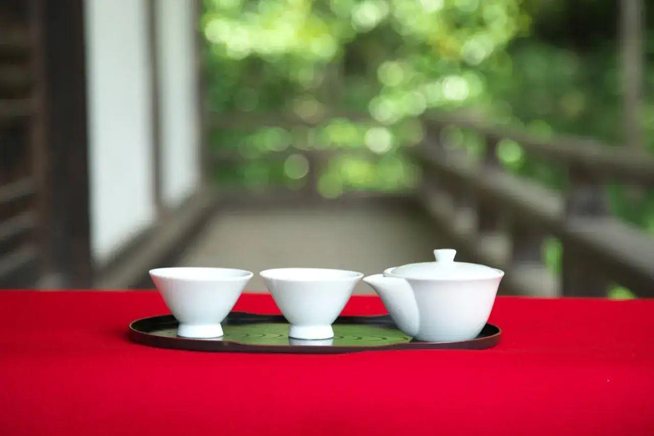 Vorbereitung f&uuml;r die Gyokuro Zubereitung: Zwei wei&szlig;e Teetassen und eine Teekanne stehen auf einem Tablett mit rotem Tuch.