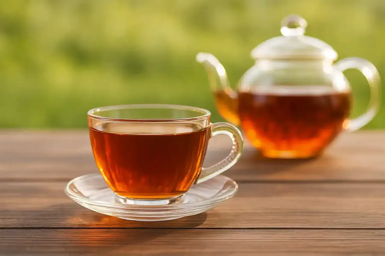 Eine Tasse und eine Teekanne mit schwarzem Tee auf einem Holztisch. Dieser schwarze Tee macht wach und belebt.