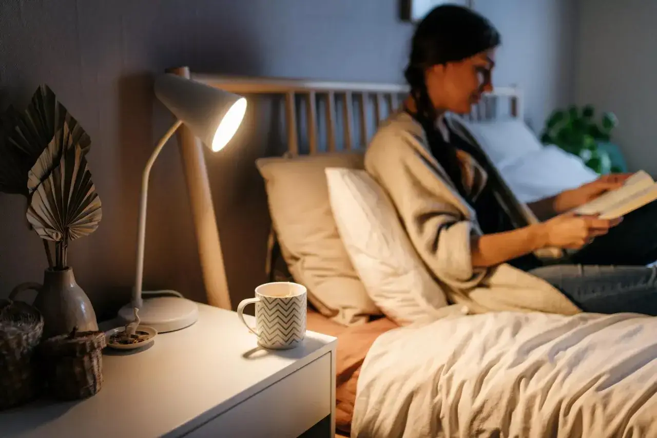 Gem&uuml;tliche Nacht: Eine Frau liest im Bett, neben ihr eine Tasse rooibos tee. Die Wirkung von rooibos tee auf den Schlaf ist entspannend.