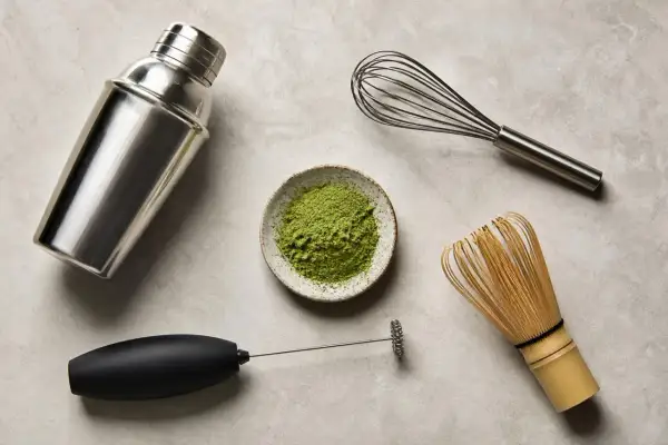 Matcha-Zubereitung: Pulver in Schale, daneben ein Milchaufschäumer, ein Schneebesen und ein Shaker. So gelingt Matcha ohne besen.