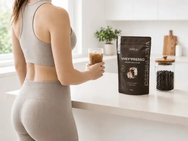 Frau hält Eiskaffee, neben VHEY® PRESSO Protein-Pulver. Die Koffein-Wirkdauer wird durch den belebenden Drink unterstützt.