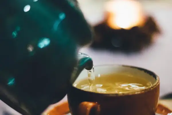 Ein grüner Teekrug gießt goldenen Tee in eine orangefarbene Tasse. Welcher Tee treibt nicht? Dieser hier, der Ruhe und Wärme verspricht.