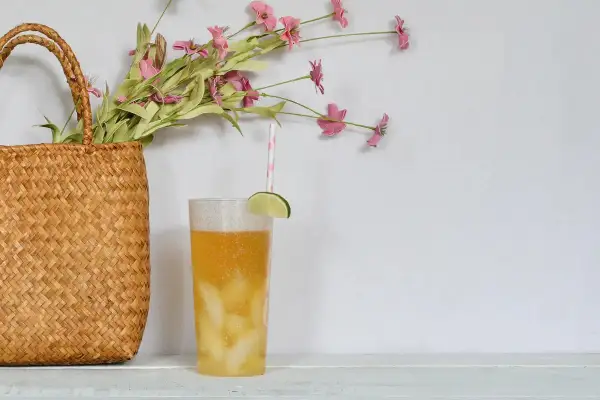 Erfrischender Drink mit Limette und Eis, daneben ein Korb mit Blumen. Perfekt, um Minztee selber zu machen und den Sommer zu genießen.