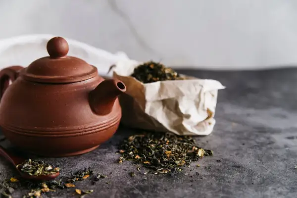 Braune Teekanne mit losem Tee und einem Löffel, bereit für den Aufguss Tee.