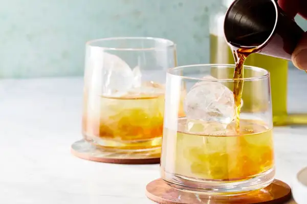 Zwei Gläser mit Eis und einem bernsteinfarbenen Getränk. Ein Jigger gießt Flüssigkeit in das vordere Glas. Ein erfrischender Gin mit Eistee.