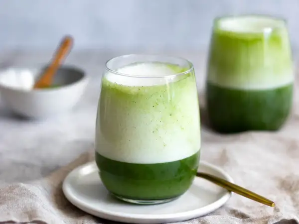 Zwei Gläser mit geschichtetem Matcha-Latte, die die perfekte Matcha-Zubereitung zeigen. Ein Löffel liegt daneben.
