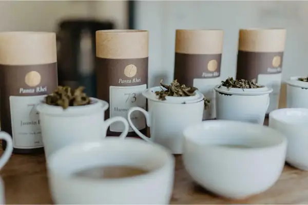 Bereit für den perfekten tee am morgen? Mehrere weiße Teetassen mit losem Tee und braune Röhren mit Teelabeln stehen bereit.