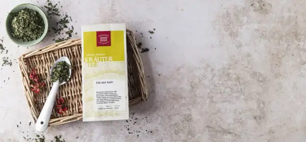 Kräutertee-Packung mit Löffel und Schale voller Kräuter. Die tee temperatur tabelle gibt Hinweise zur Zubereitung.