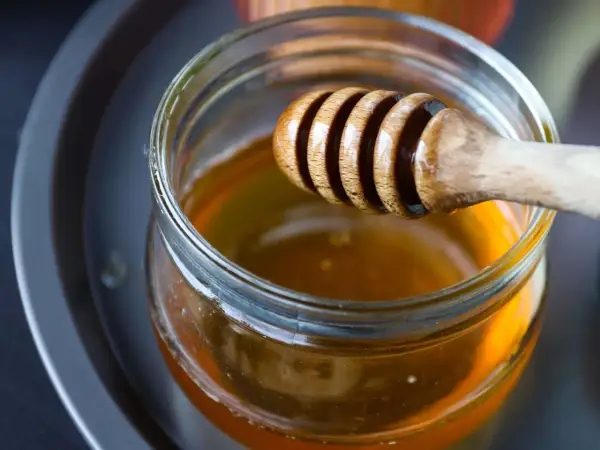 Ein Holzlöffel taucht in ein Glas mit flüssigem Honig. Perfekt zum Süßen von Tee.