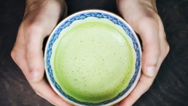 Hände halten eine Schale mit schaumigem, leuchtend grünem Matcha. Für manche ist Matcha ein Genuss, für andere ein Thema bei Histaminintoleranz.