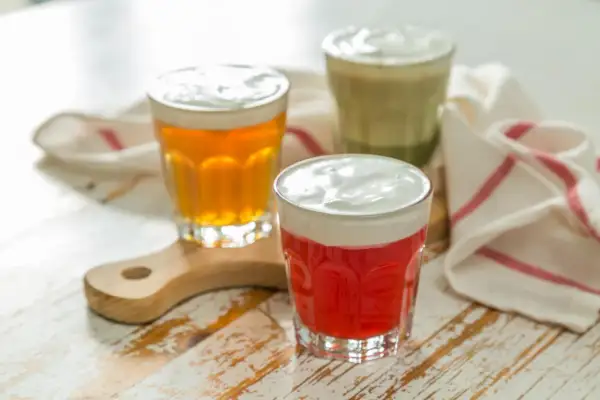 Drei Gläser mit bunten Getränken und cremiger Käseschaumhaube. Ein rotes, ein bernsteinfarbenes und ein grünes Cheese Tea.