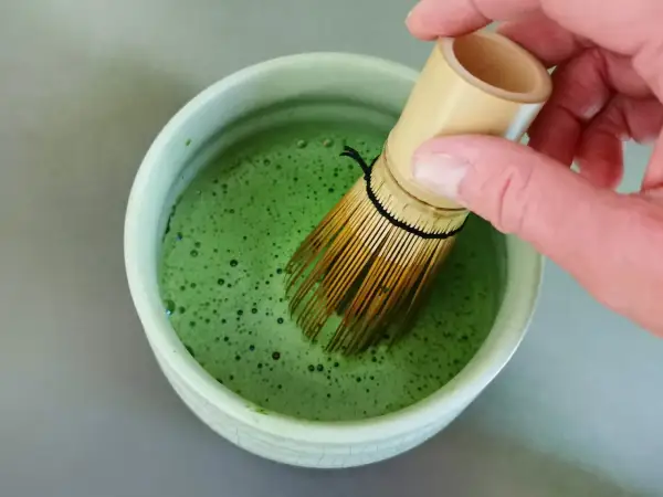 Hand whisking bright green matcha in a bowl. The ideal matcha temperatur is crucial for a smooth, frothy brew.