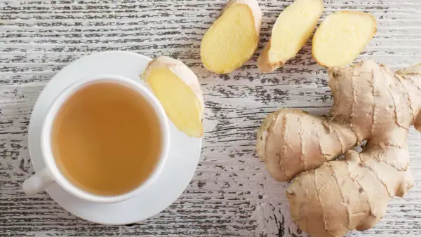 Eine Tasse Ingwertee und frische Ingwerstücke auf holzigem Hintergrund. Perfekt für einen beruhigenden Ingwer abends.