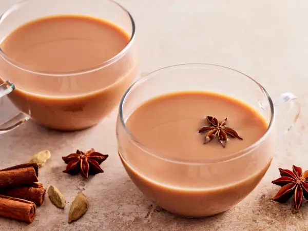 Zwei Tassen cremiger Chai Latte, garniert mit Sternanis. Zimtstangen und Kardamomkapseln deuten auf ein authentisches indischer chai rezept hin.